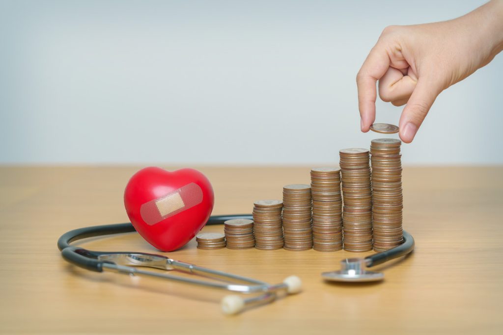A hand putting money on a stack surrounded by a stethoscope